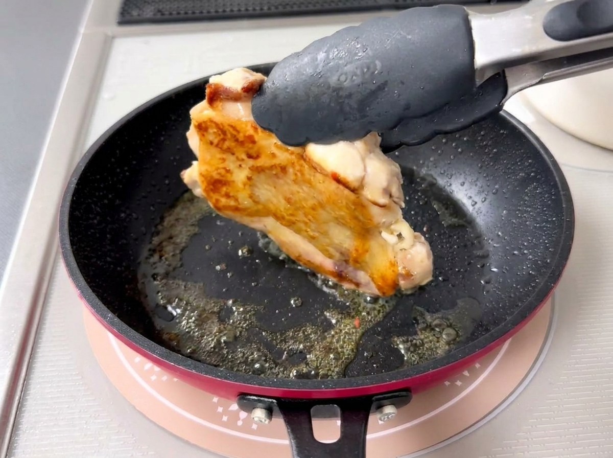Gros plan dune pince retournant un morceau de poulet pour révéler une peau parfaitement dorée et croustillante.