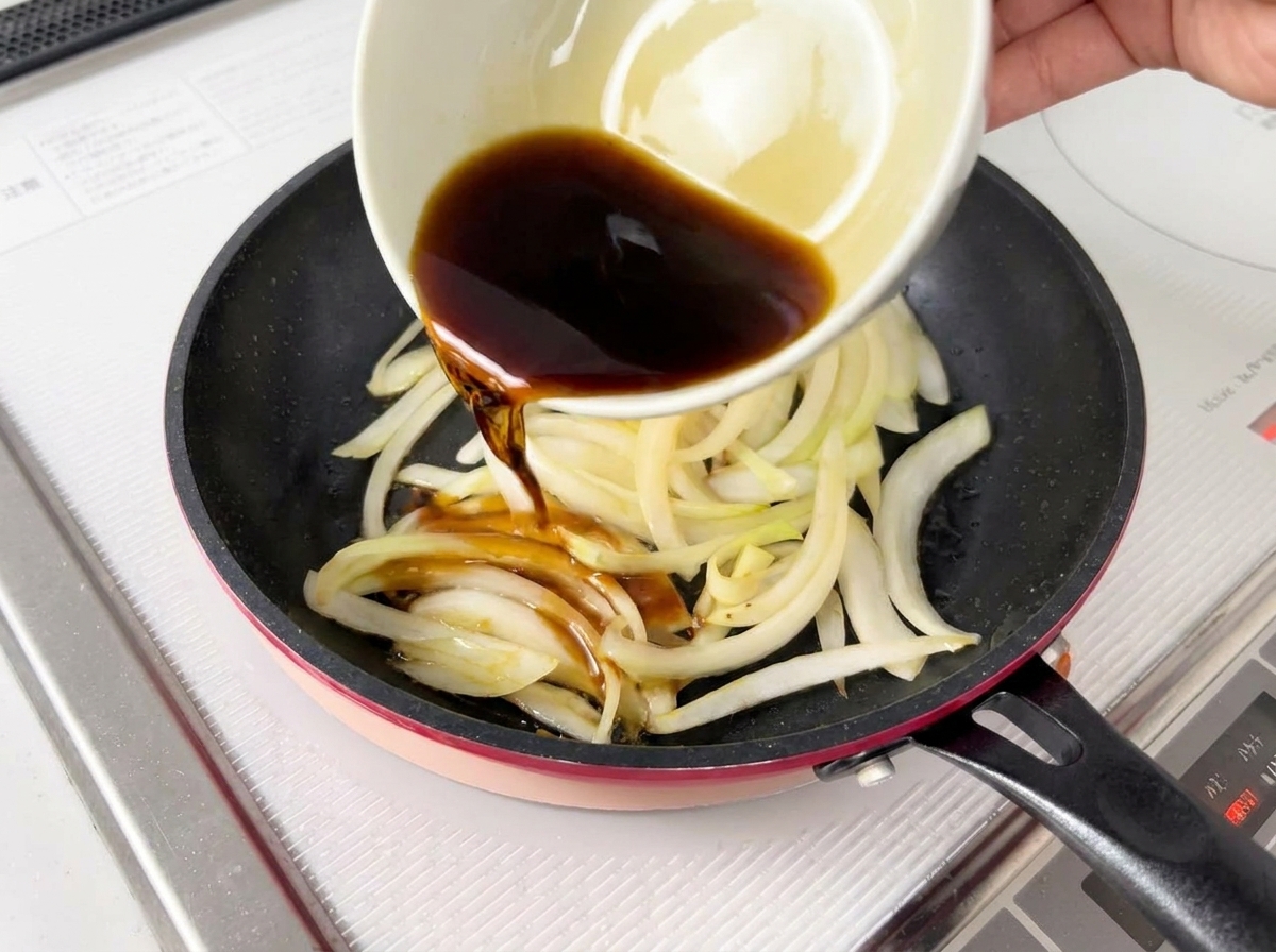 Sauce sombre versée depuis un bol blanc sur des oignons ramollis dans une poêle.
