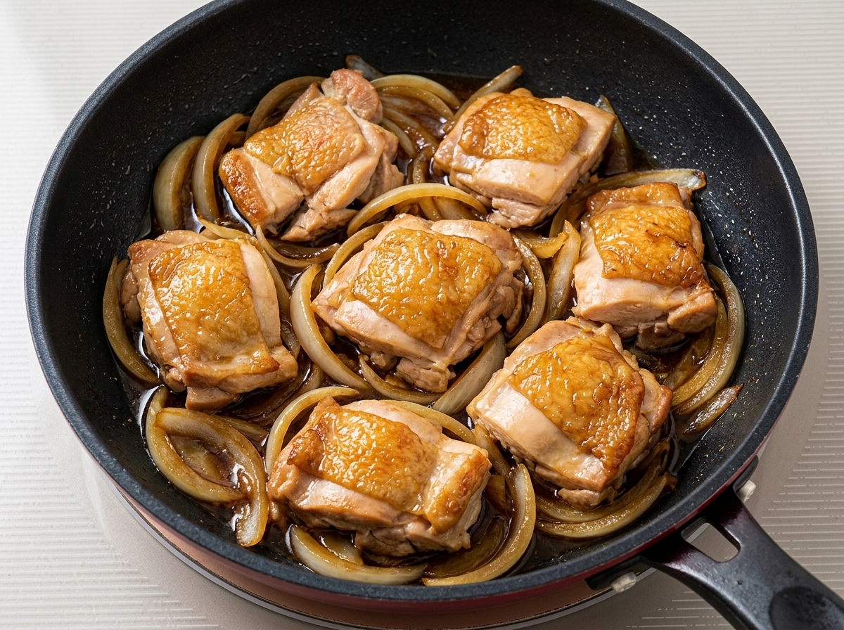 Morceaux de poulet poêlés mijotant avec des oignons et de la sauce sombre dans une poêle.