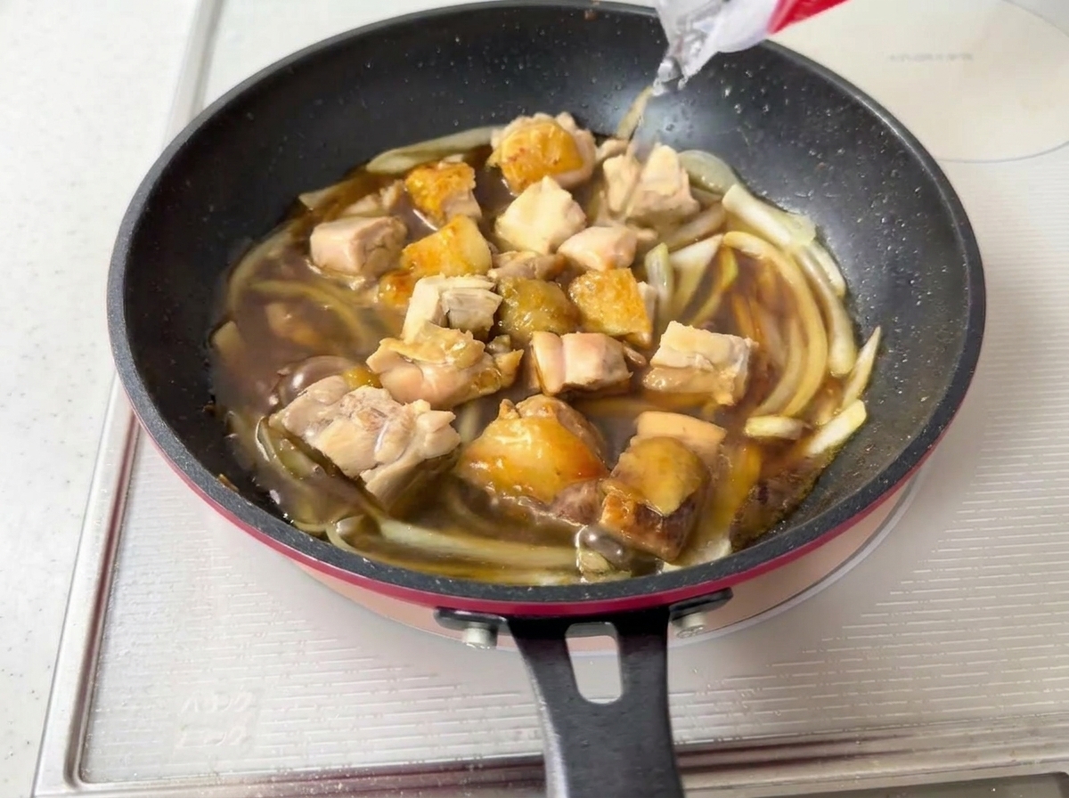 De leau versée dans une poêle contenant le poulet, les oignons et la sauce sombre mijotant.