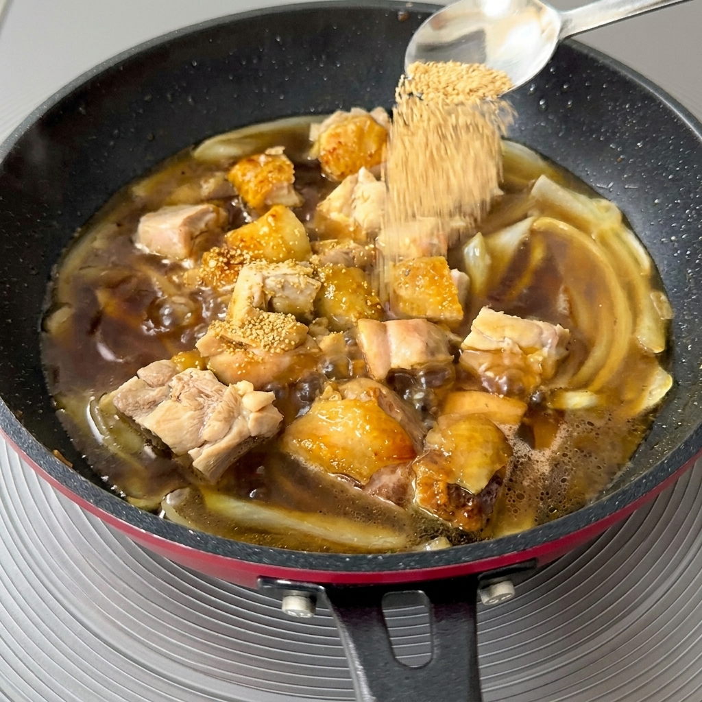Gros plan dune cuillère remplie de granulés de dashi dorés saupoudrés dans une poêle mijotante de poulet et doignons.