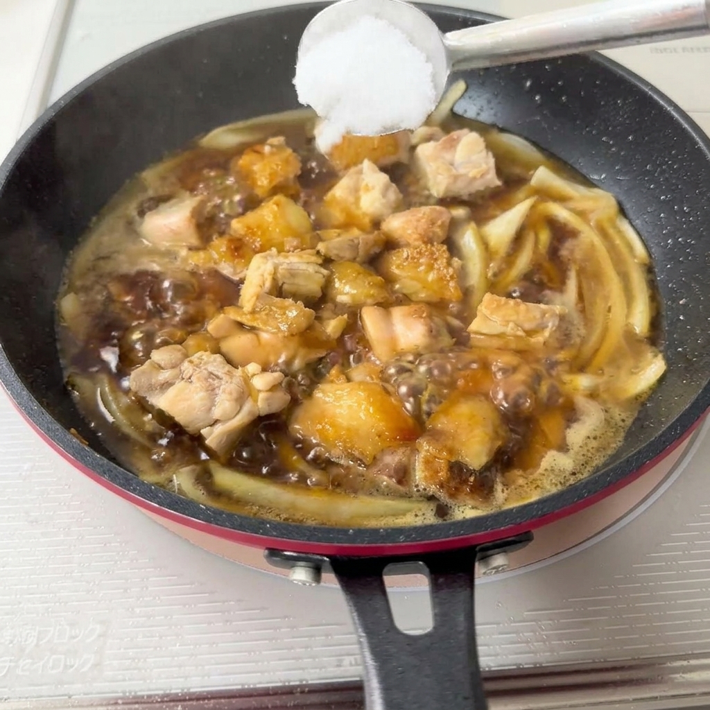 Une cuillère en métal contenant un monticule de sucre blanc en train dêtre abaissée dans la poêle de cuisson.