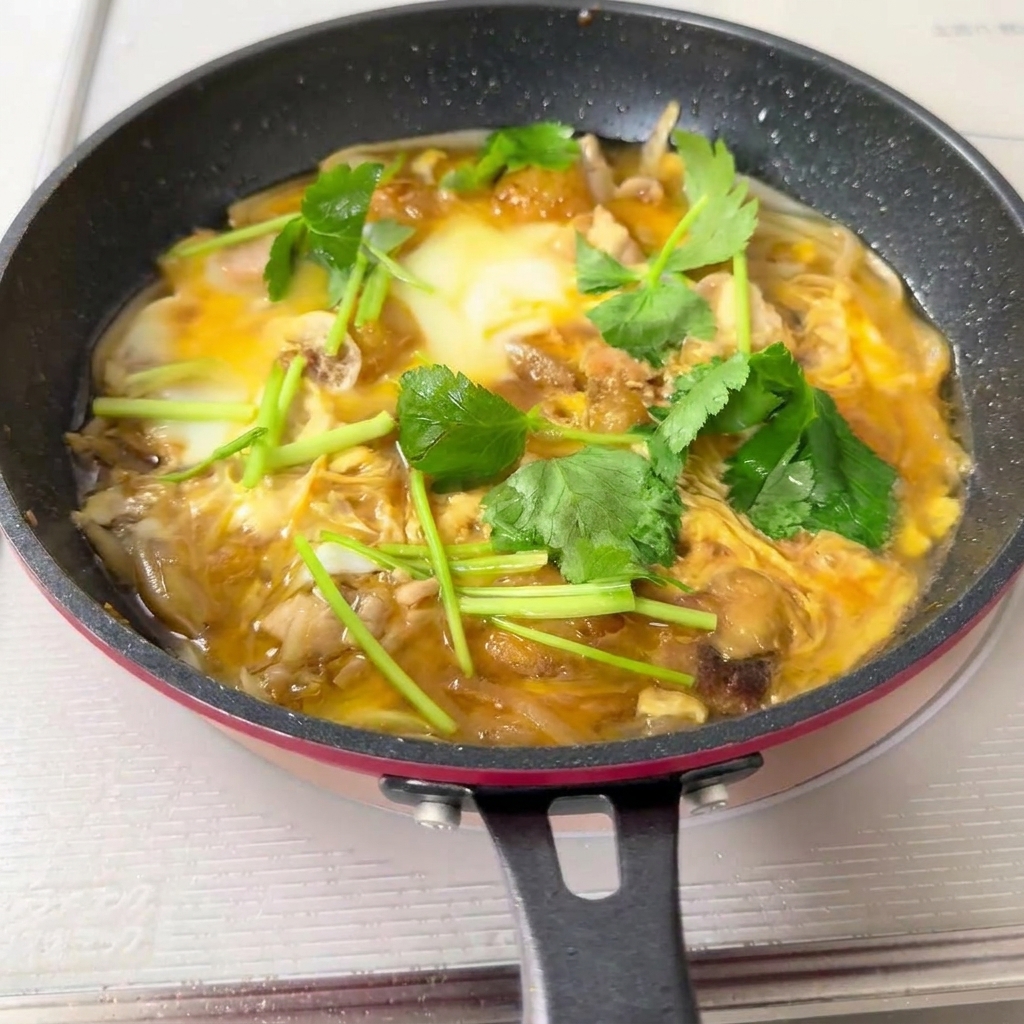 Une poêle remplie du mélange Oyakodon cuit étant versé sur un bol de riz blanc vapeur.