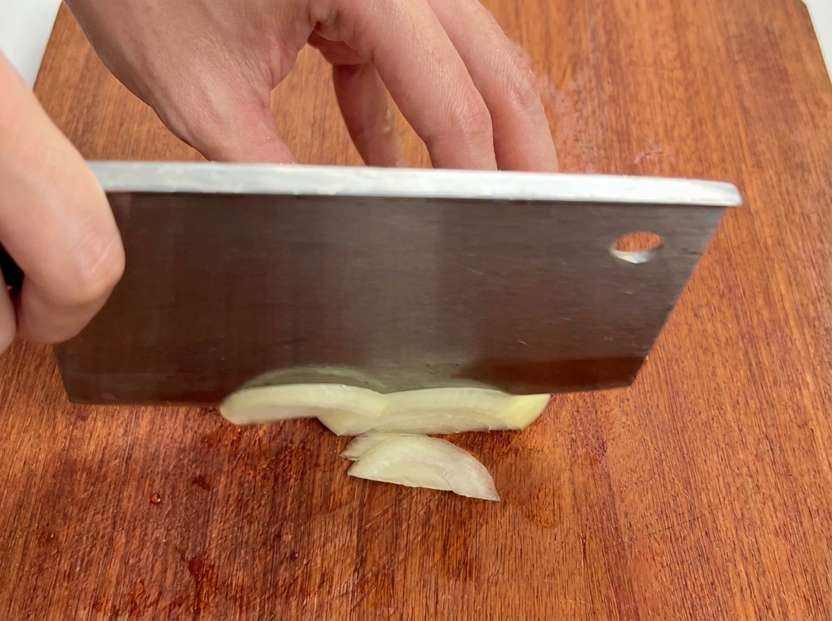 Gros plan sur un oignon blanc coupé en fines lamelles sur une planche à découper en bois.