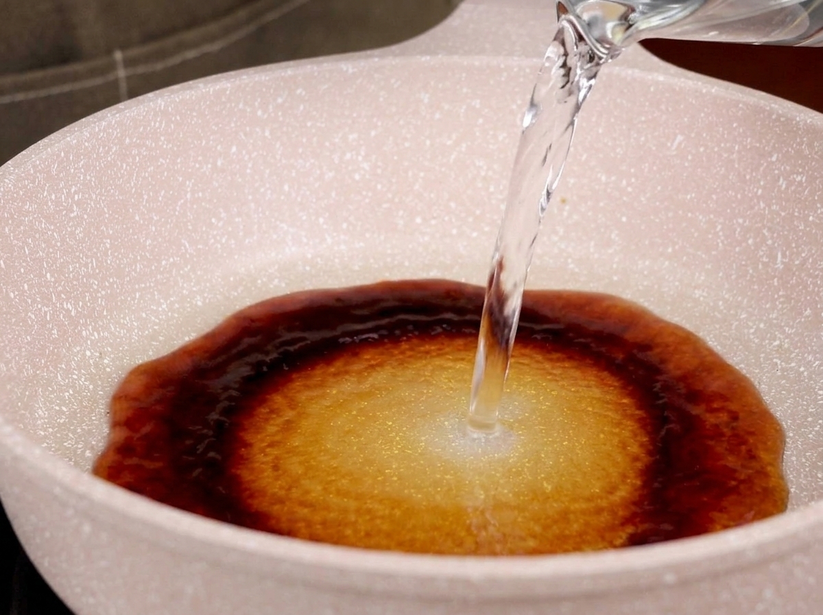 De leau versée dans une poêle contenant de la sauce teriyaki pour former un bouillon.