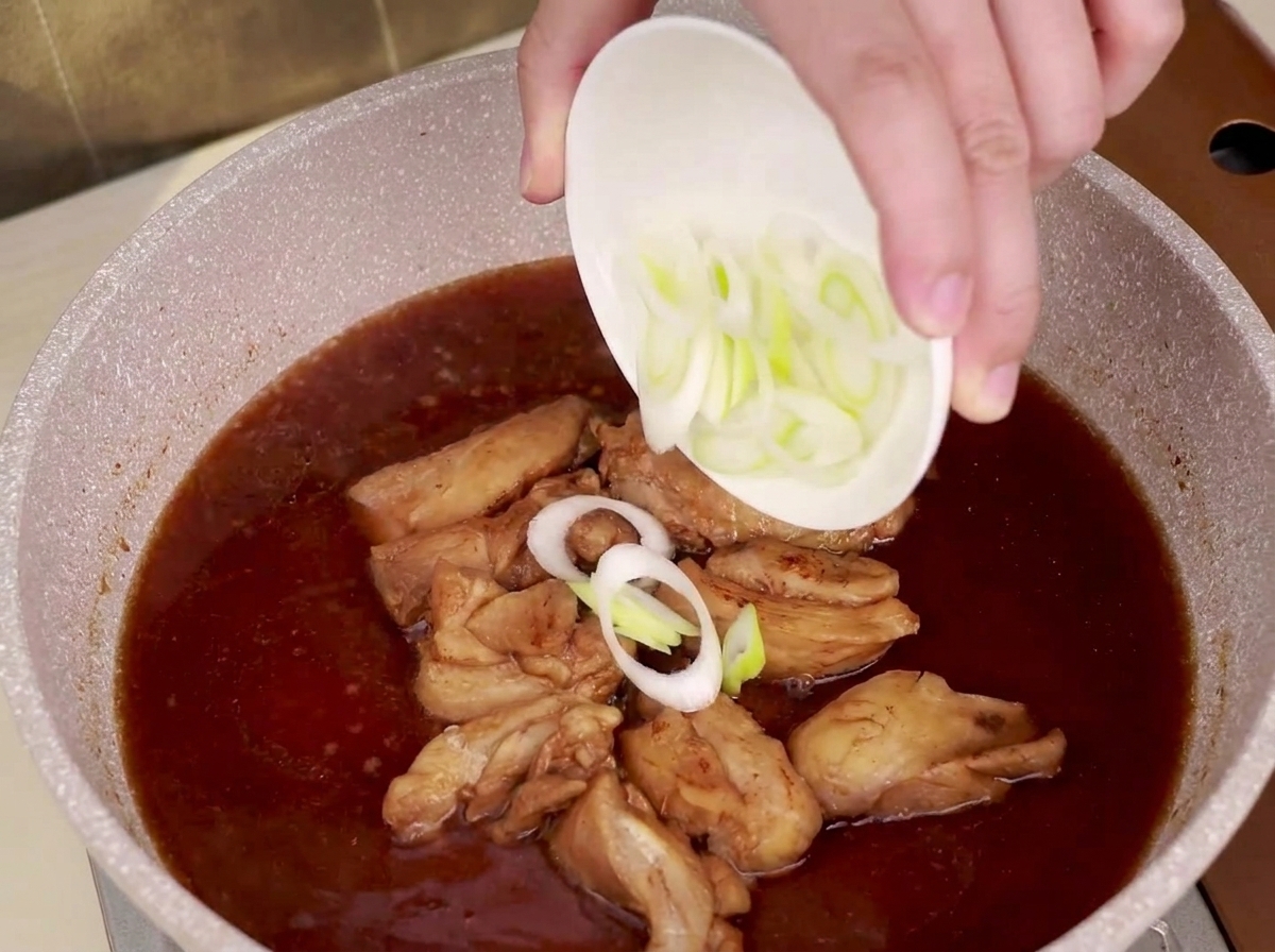 Rondelles de poireau saupoudrées dans une poêle où mijotent le poulet et la sauce teriyaki.
