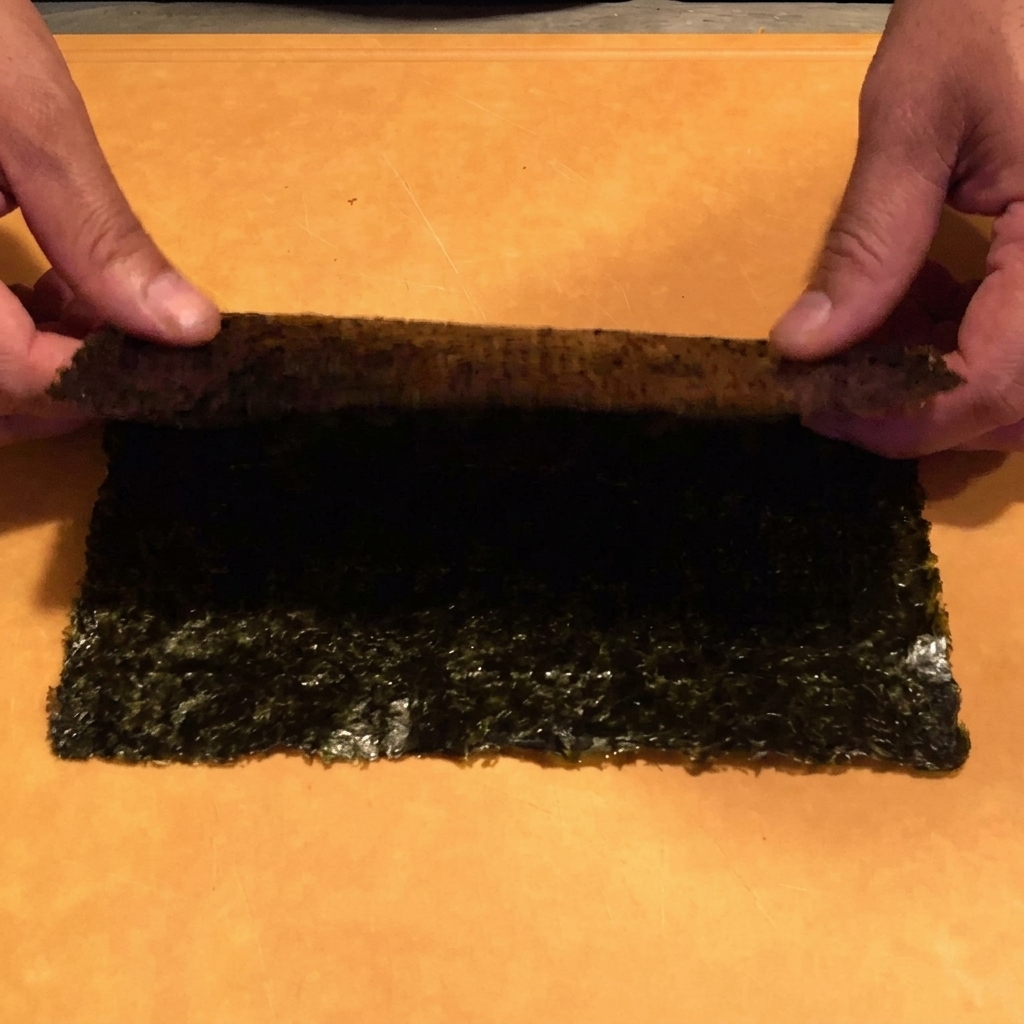 Gros plan sur des mains utilisant des ciseaux de cuisine pour couper une feuille de nori en fines lanières au-dessus dun bol.