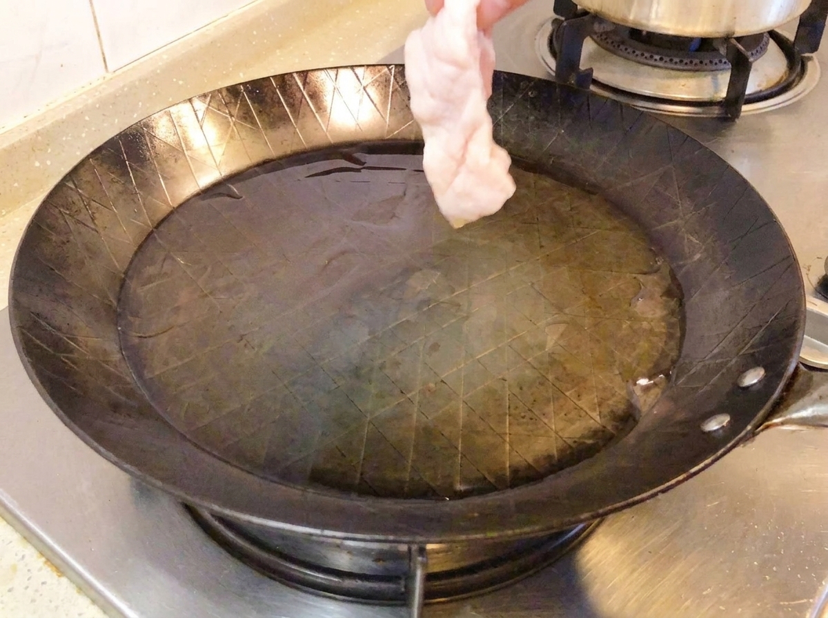 Cuisse de poulet crue placée côté peau dans une poêle chaude.