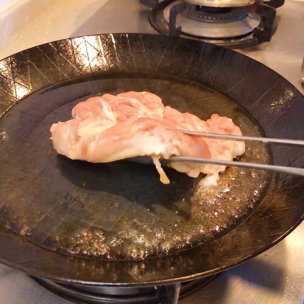 Des pinces soulevant le poulet dans une poêle pour révéler une peau dorée et croustillante.