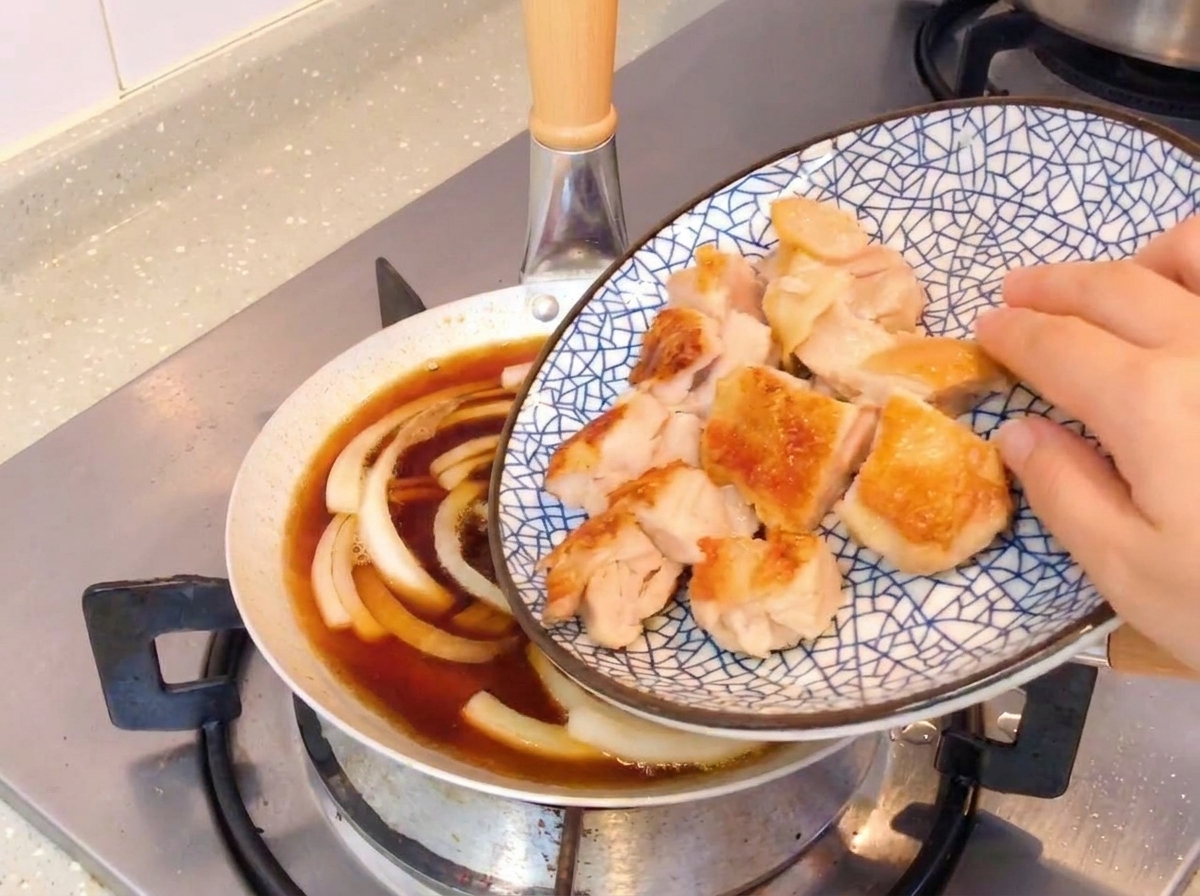 Tranches de poulet poêlé croustillant ajoutées dans une poêle avec des oignons frémissants et une sauce à base de soja.