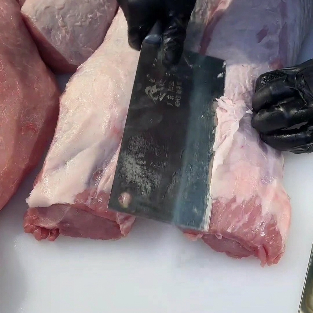 Vue rapprochée dun couperet à viande retirant lexcès de gras dun morceau de filet de porc cru.