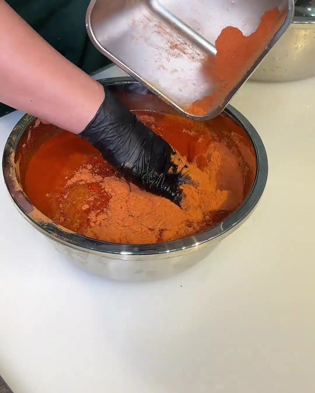 Un bol rempli de sauce marinade rouge, avec une main gantée remuant les tranches de porc pour les enrober uniformément.