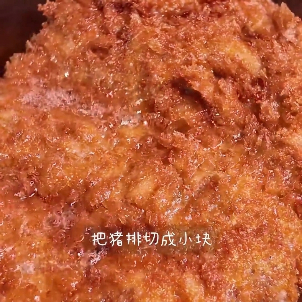 Une côtelette de porc frite dorée étant tranchée en lanières sur une planche à découper en bois.