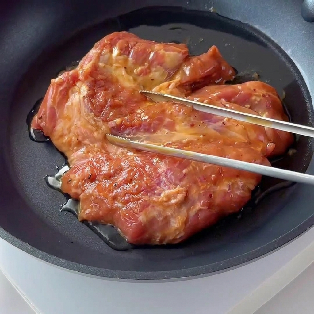 Une côte de porc assaisonnée grésillant et dorant dans une poêle antiadhésive sombre.