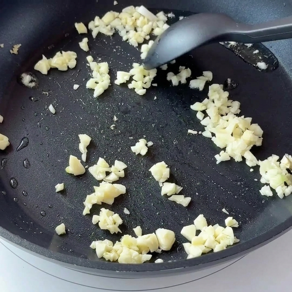 Ail haché et oignons en dés rissolant dans une poêle antiadhésive sombre.