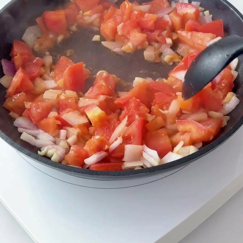 Tomates et oignons rouges en dés sautés dans une poêle, en y mélangeant le concentré de tomate.