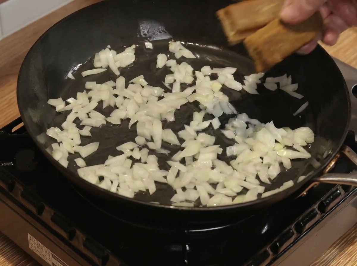 Des carrés de curry et de leau mélangés avec des oignons revenus dans une poêle.