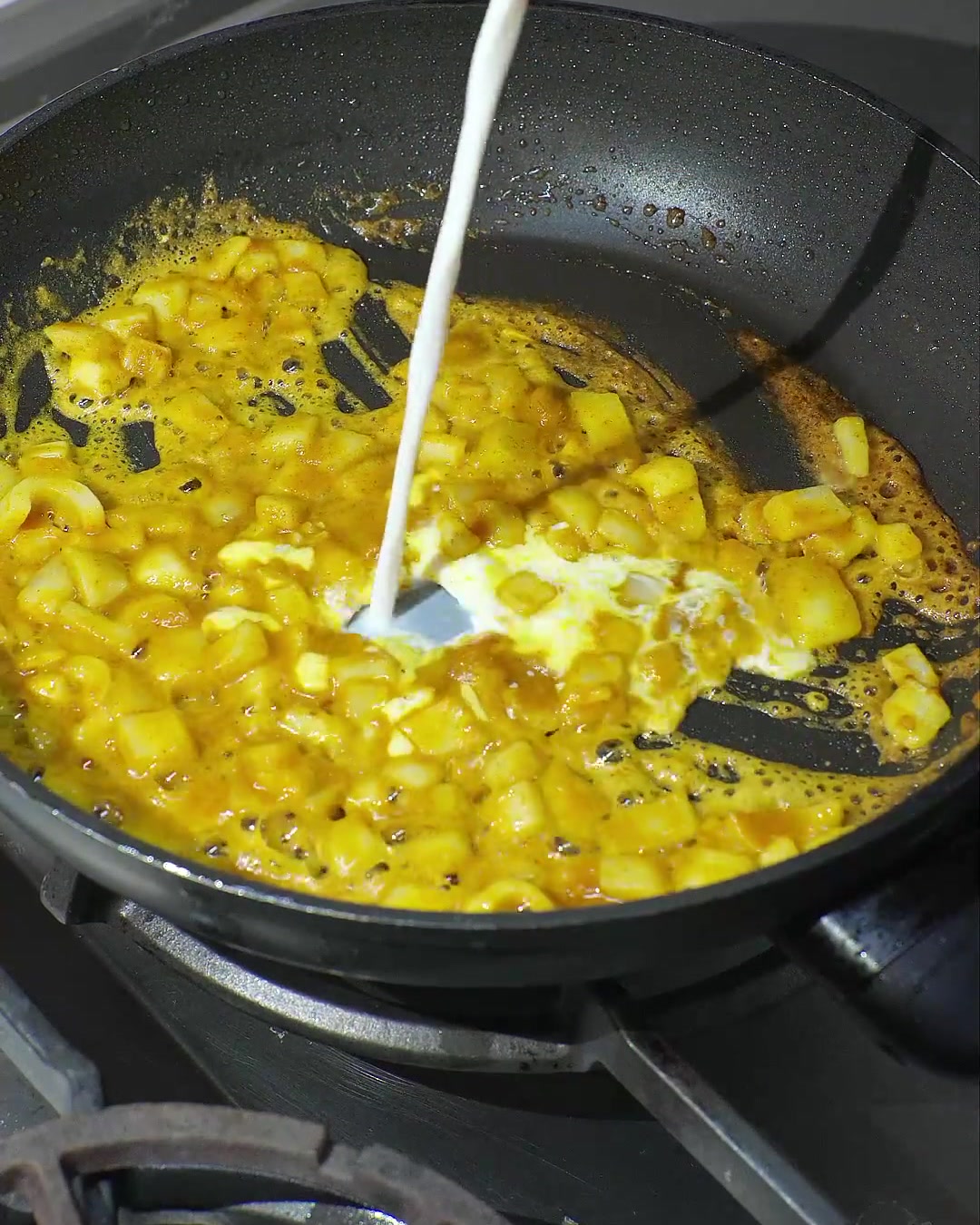 Du lait de coco versé dans une poêle contenant du curry fondu et des oignons sautés, créant une sauce jaune crémeuse.