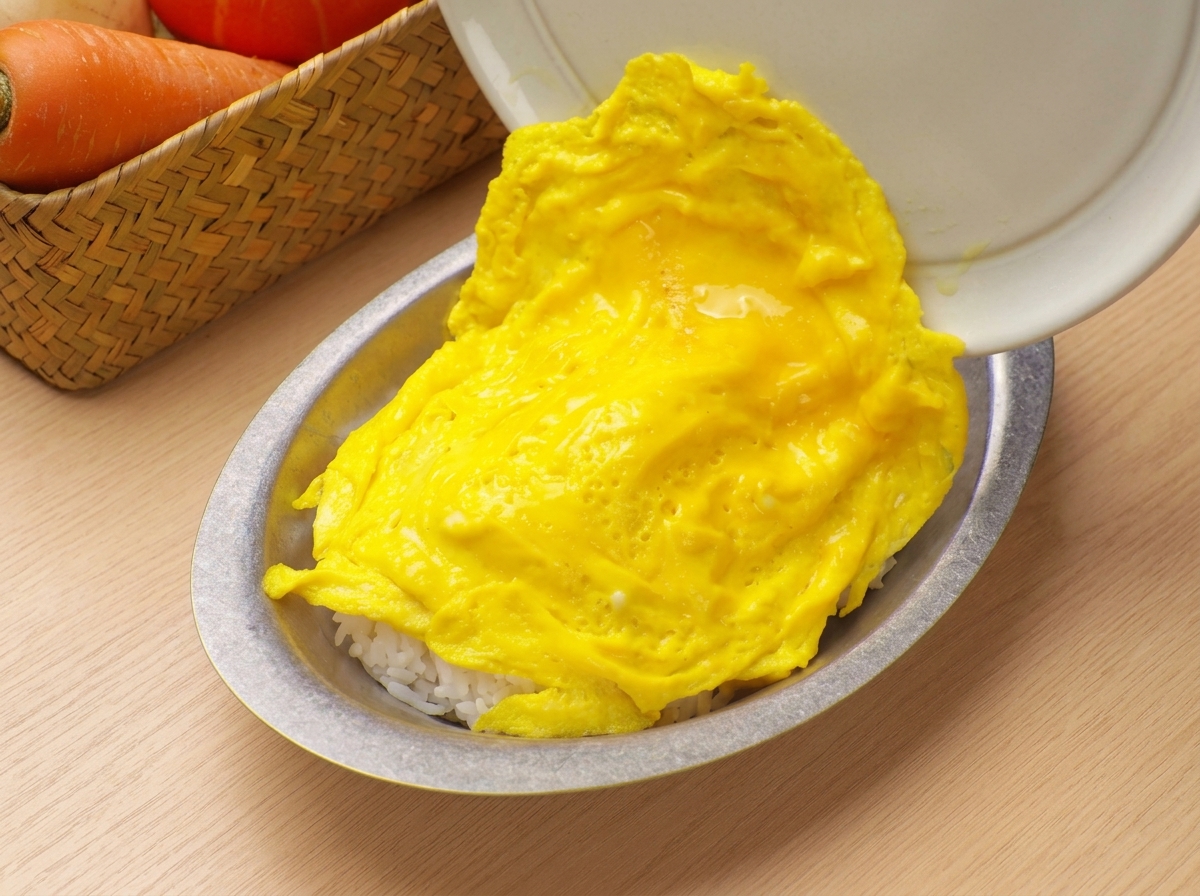 Des œufs brouillés moelleux glissant dune poêle vers un bol de service rempli de riz blanc.