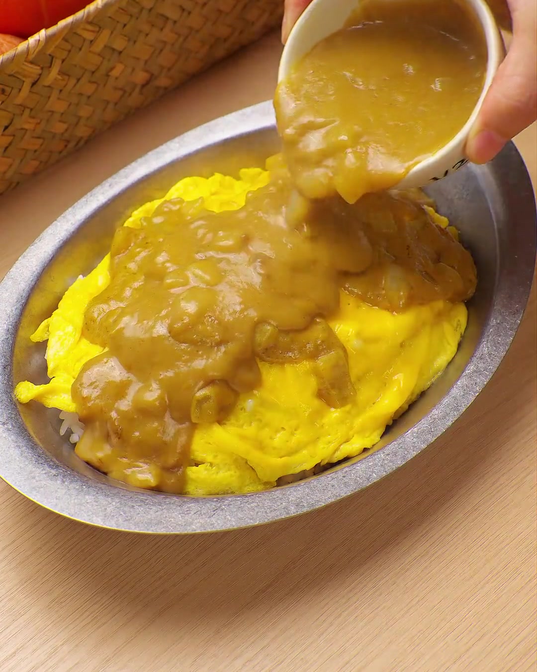 Une sauce curry jaune et riche versée depuis un petit bol sur un lit dœufs brouillés et de riz.