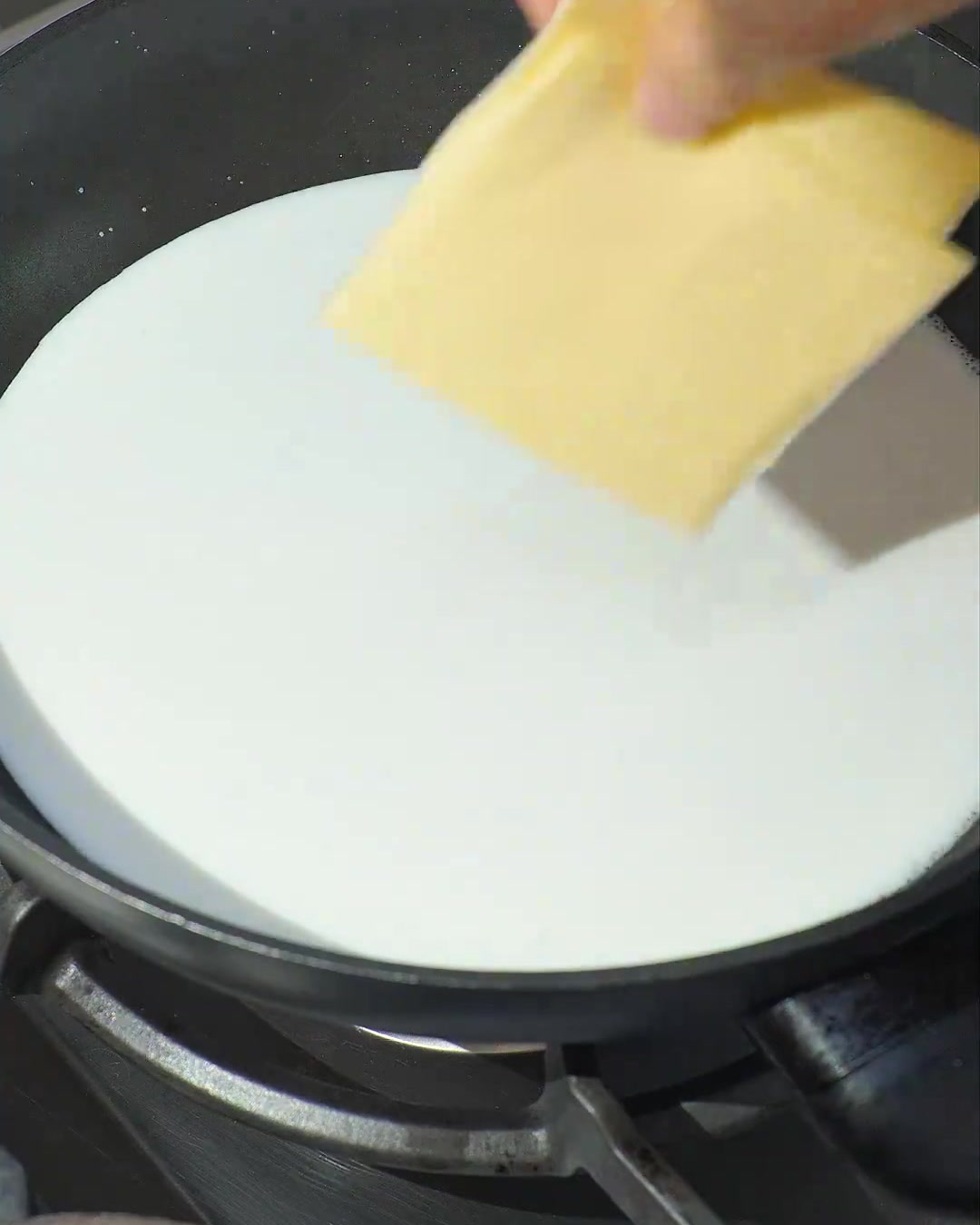 Deux tranches de fromage jaune fondant dans du lait de coco blanc frémissant dans une poêle sombre.