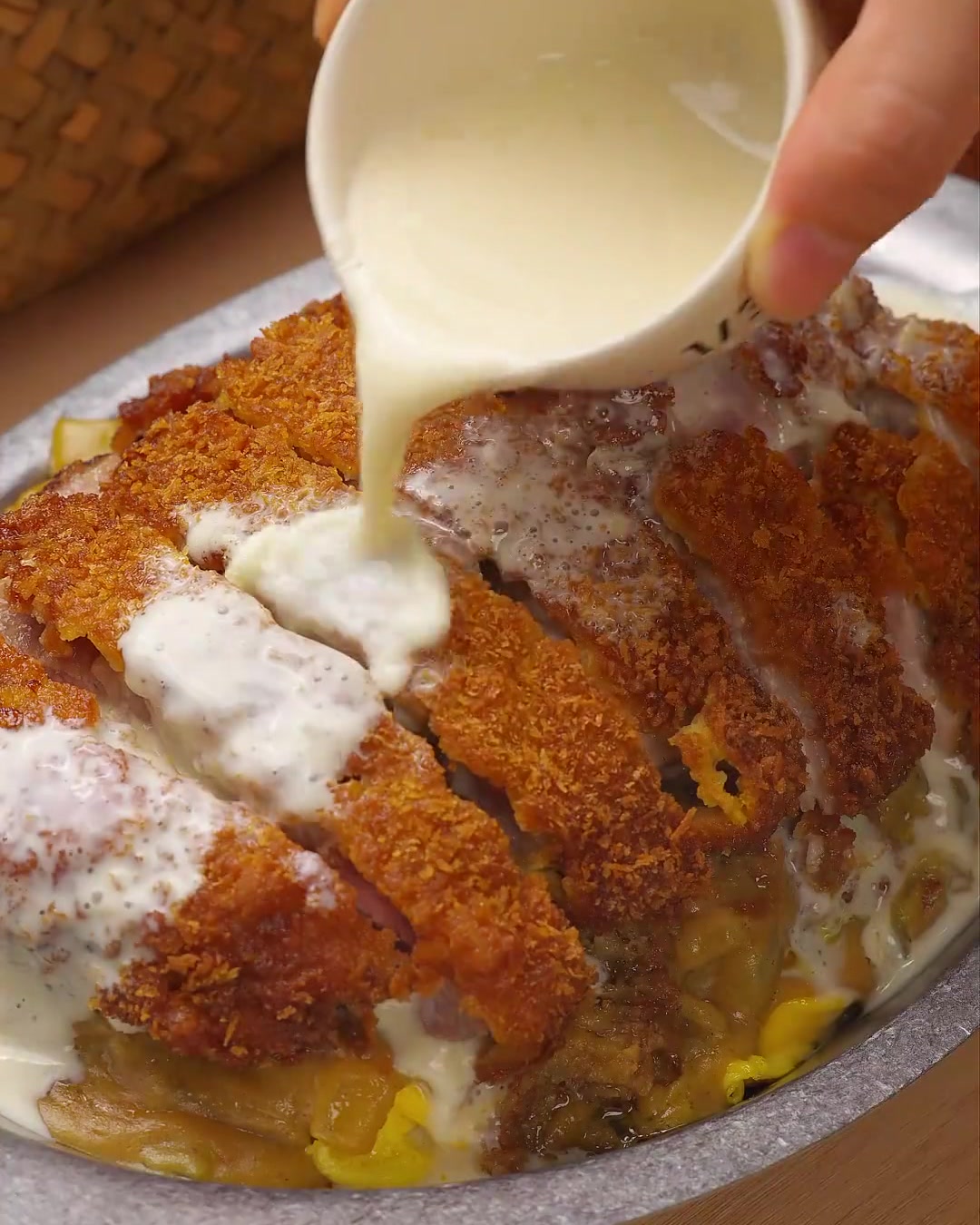 Gros plan sur une sauce crémeuse blanche au fromage et au coco versée sur des tranches de côtelette de porc dorées, garnies de persil frais.