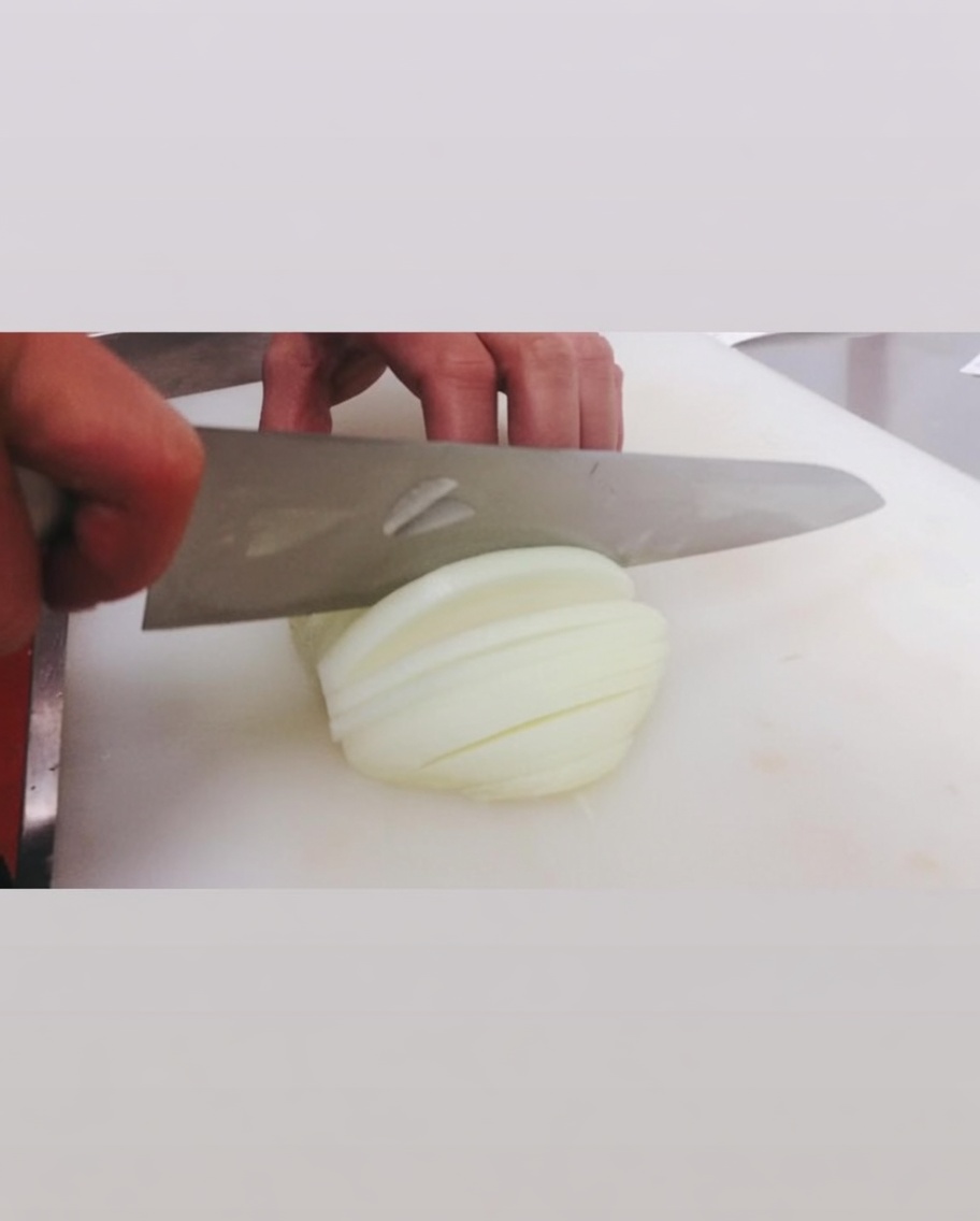 Tranchage dun oignon blanc cru avec un grand couteau sur une planche à découper blanche.