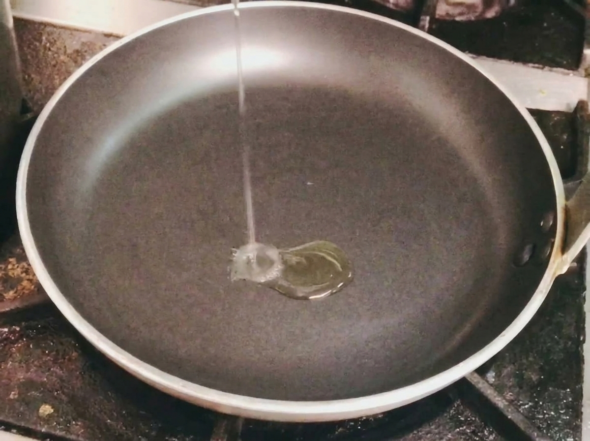 Un mince filet dhuile de cuisson versé dans une poêle noire vide sur une cuisinière.