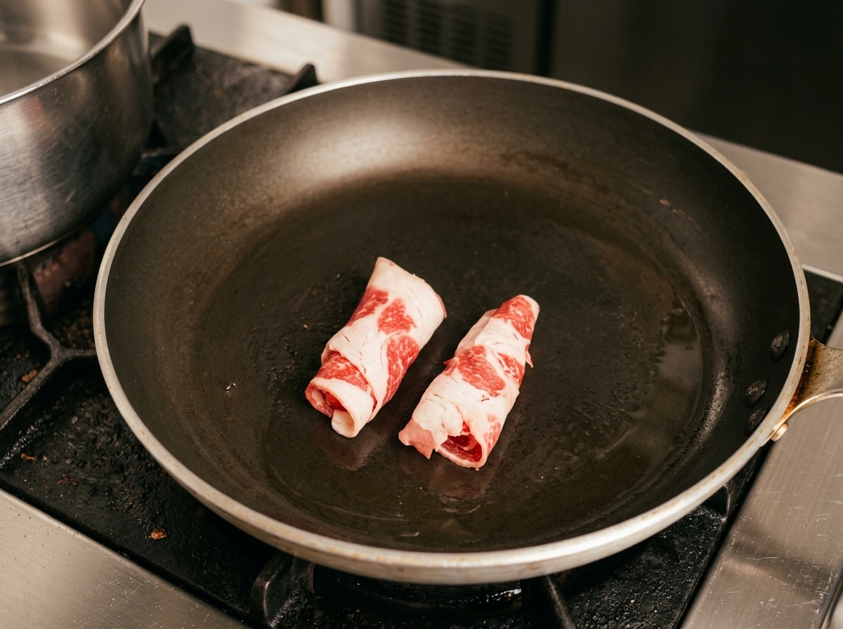 Tranches roulées de bœuf gras cru saisies dans une poêle chaude.