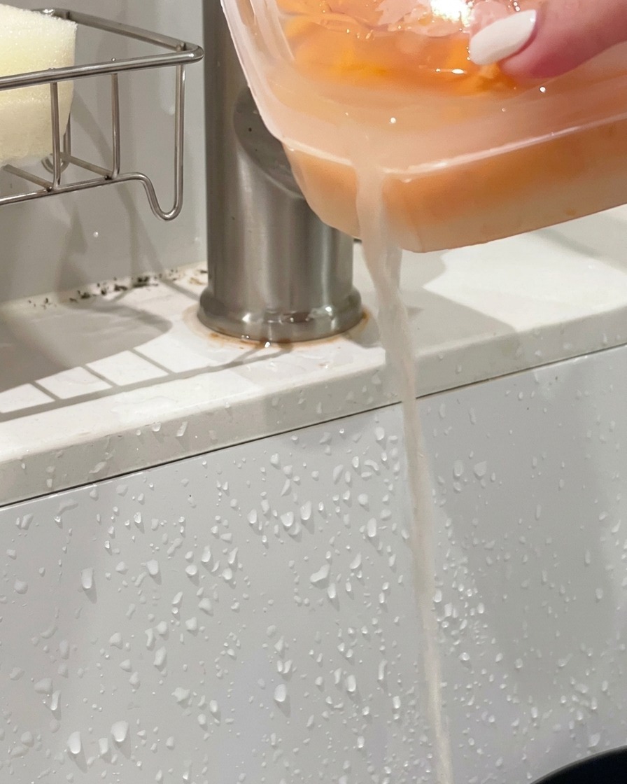 Récipient en plastique rempli doursin orange incliné au-dessus dun évier pour vider le liquide.