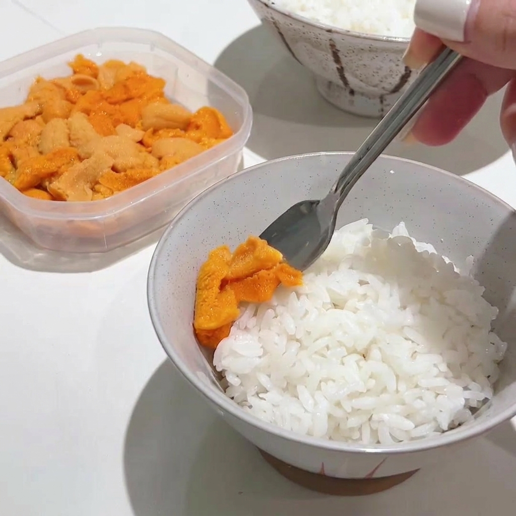 Une cuillère en métal déposant délicatement une généreuse portion doursin orange vif sur un bol de riz blanc chaud.