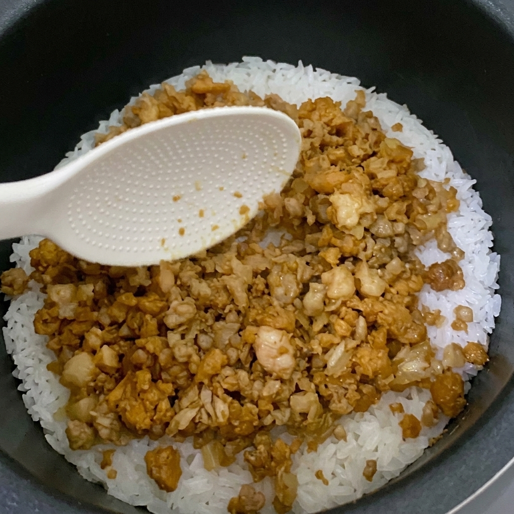 Mélange versé sur le riz dans le cuiseur à riz.