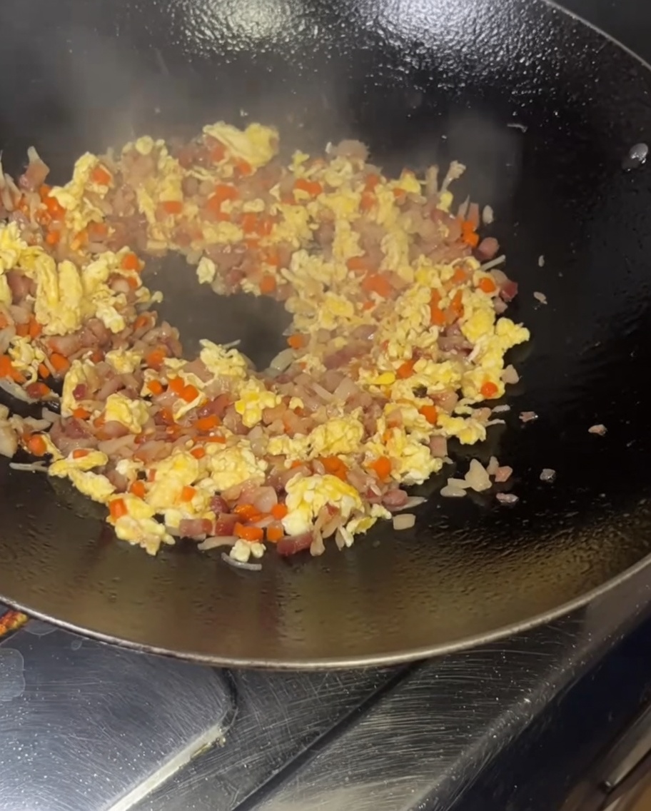 Le riz enrobé de jaune dœuf est versé dans le wok chaud.