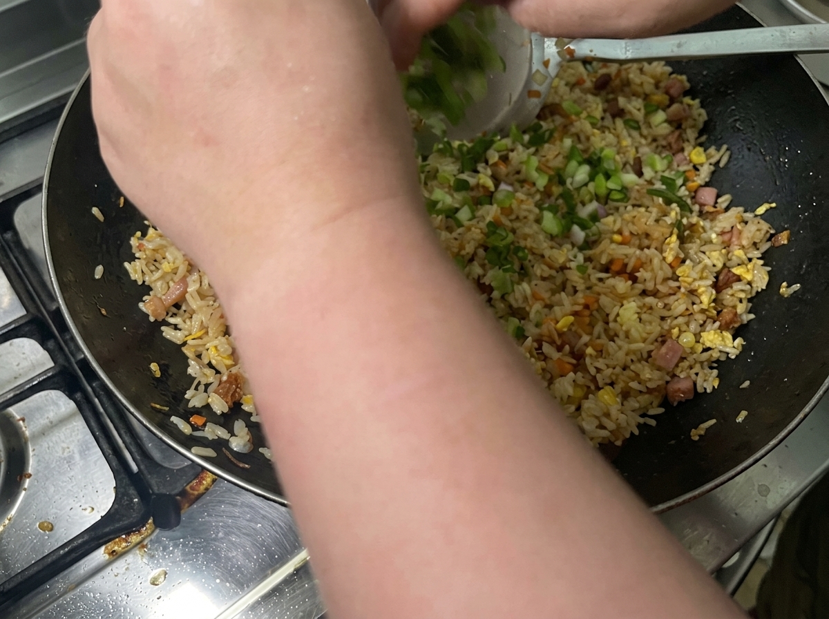 Les oignons verts hachés sont ajoutés au riz dans le wok.