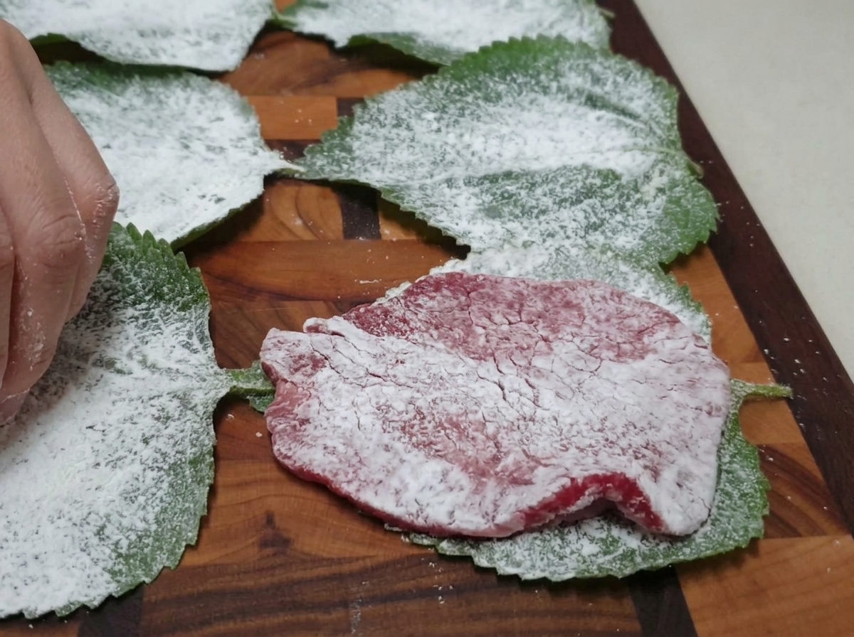 Une tranche de bœuf farinée déposée sur une feuille de perilla verte farinée, sur une planche à découper en bois.