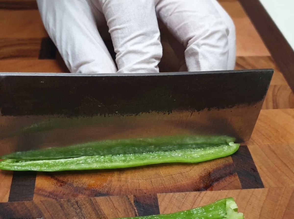Un couteau de chef hachant finement un piment vert sur une planche à découper en bois.