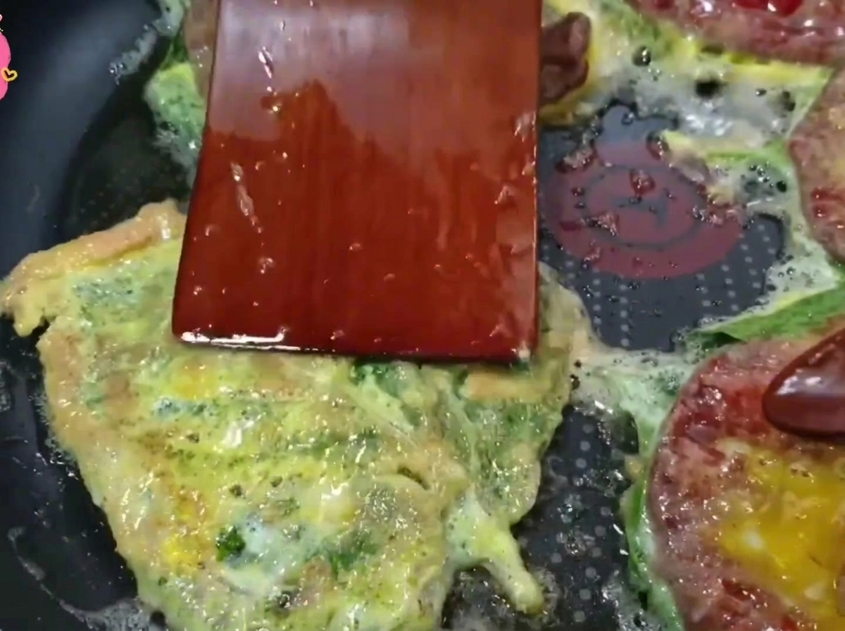 Une spatule en bois retournant une galette de bœuf dorée dans une poêle chaude.
