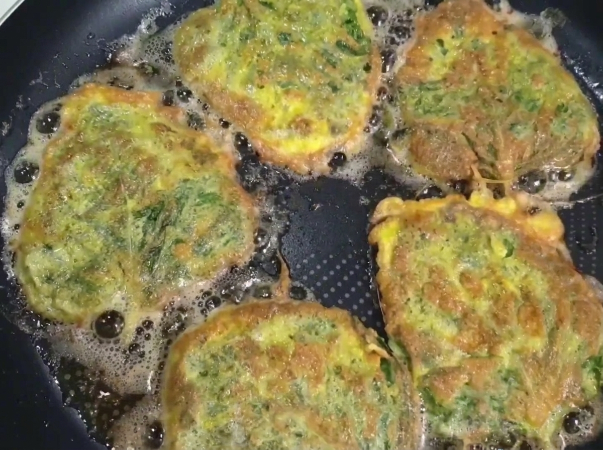 Une galette de bœuf à la perilla cuite, soulevée de la poêle à laide dune spatule et de baguettes.
