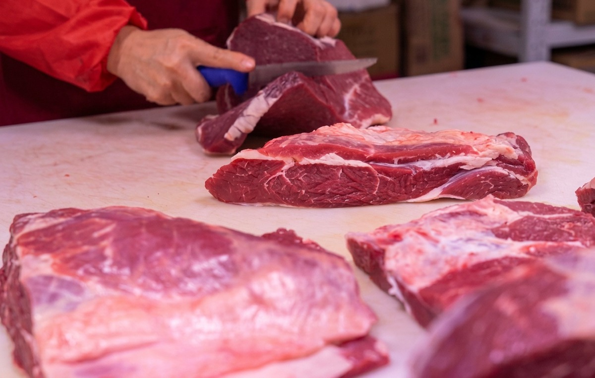 Des mains utilisant un couteau bien aiguisé pour trancher de la viande rouge sur une planche à découper blanche.