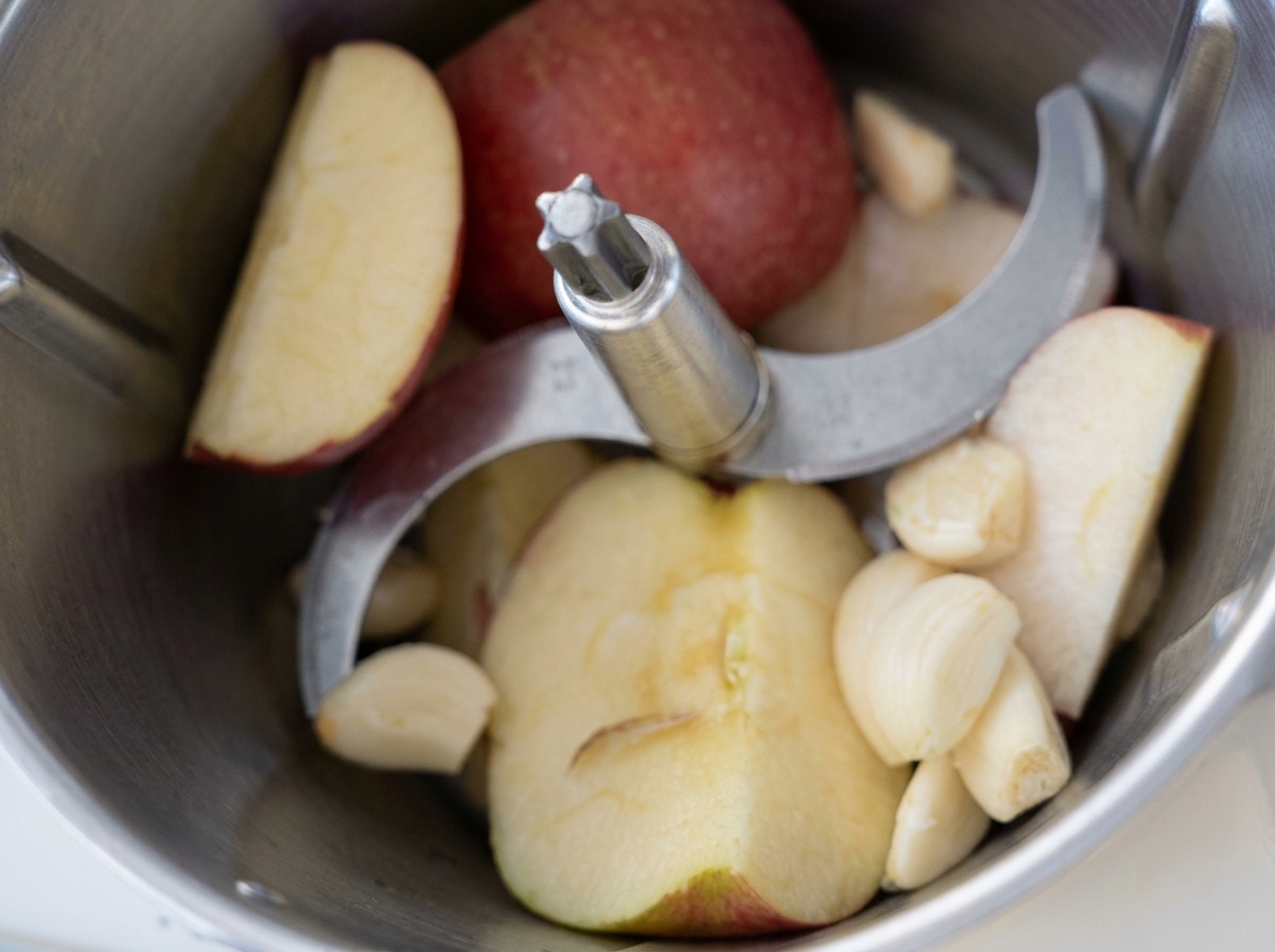 Morceaux de pomme et gousses dail pelées dans le bol dun robot culinaire avant dêtre mixés.