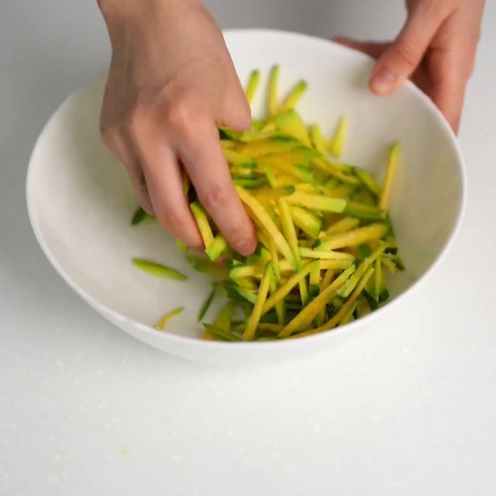 Mains pressant des lamelles de courgette salées pour égoutter le liquide dans un bol propre.