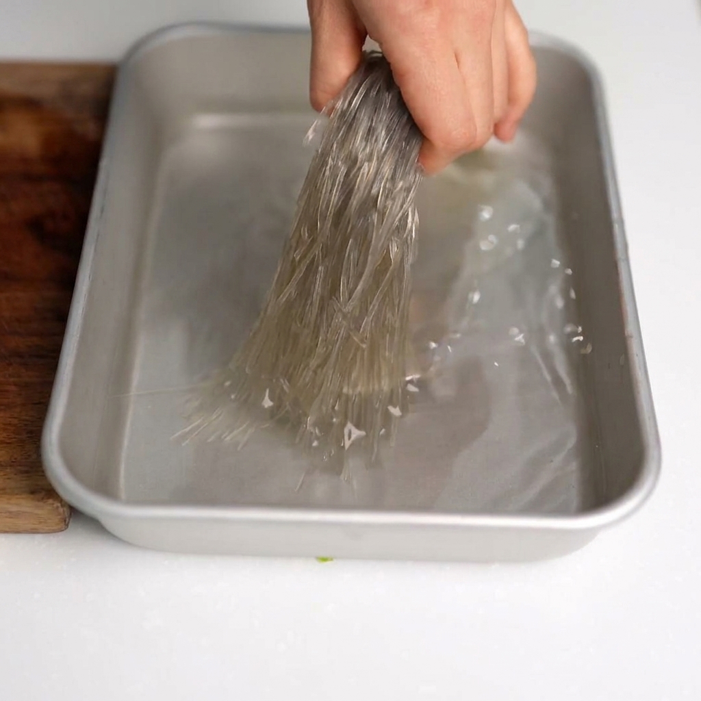 Ciseaux de cuisine coupant des nouilles de verre trempées en petits segments dans un saladier.