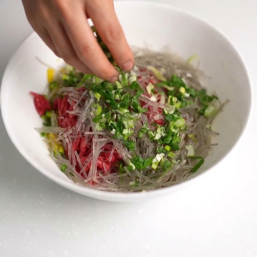 Un bol contenant du bœuf, des courgettes, des nouilles, des oignons verts, de la sauce huître et trois œufs crus.