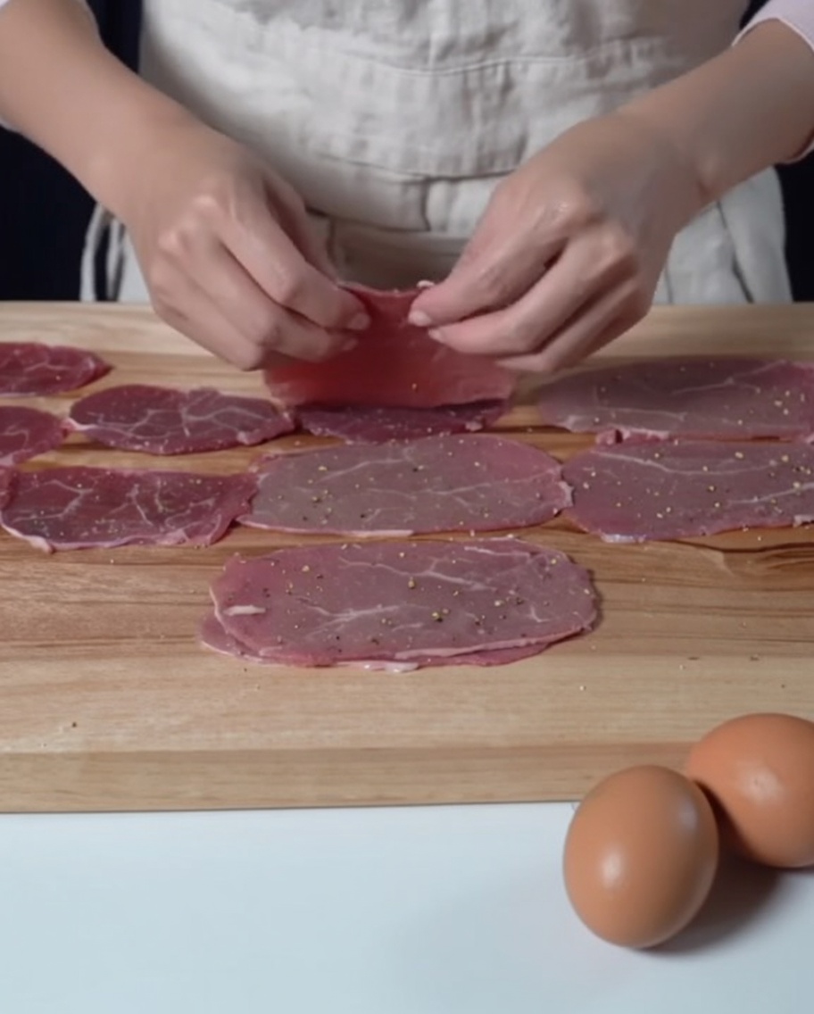 Tranches de bœuf assaisonnées disposées sur une planche à découper en bois, prêtes pour létape de la farine.