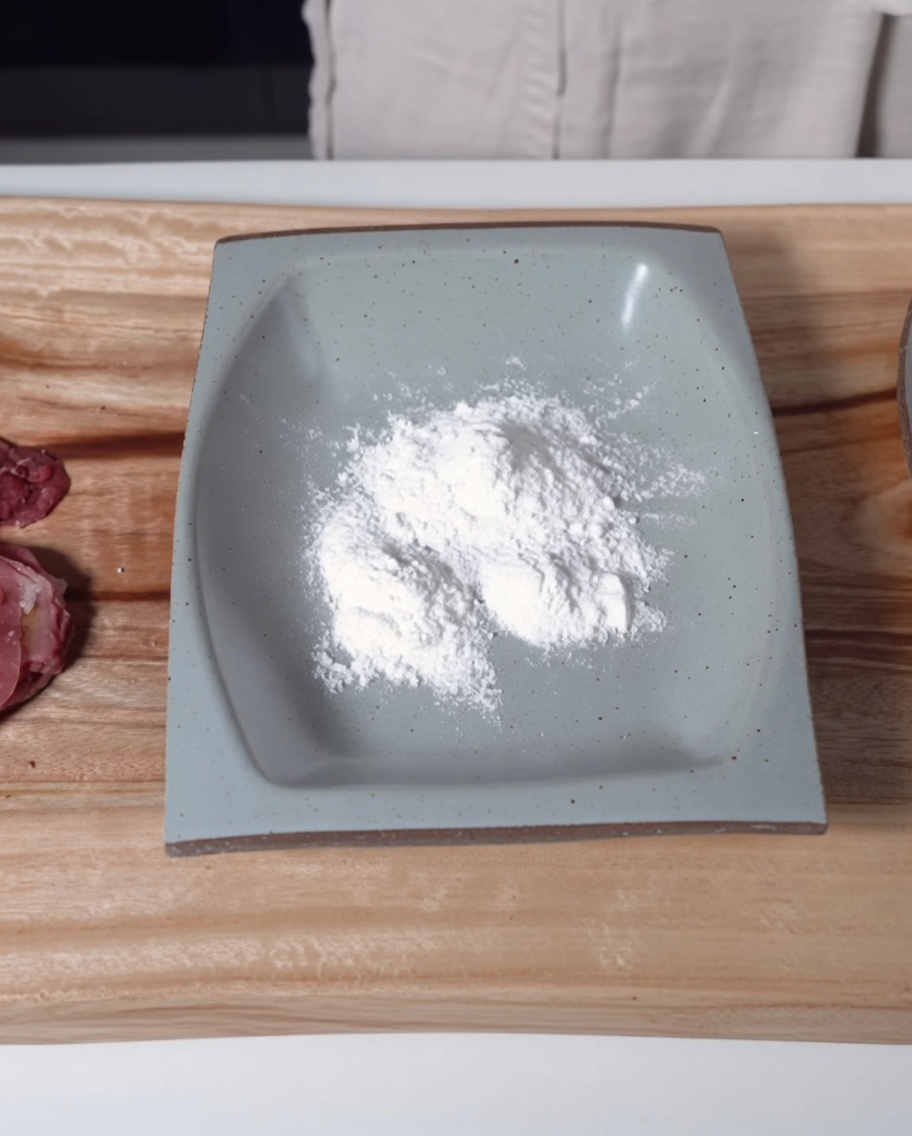 Un plat rectangulaire gris peu profond rempli de fine farine de riz gluant à côté des tranches de bœuf.