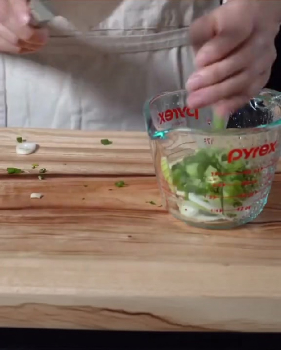 Oignons et oignons verts hachés mélangés dans une sauce sombre à lintérieur dun verre doseur.