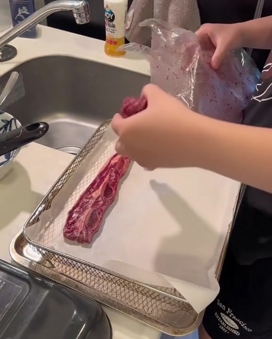 Côtelettes de bœuf crues disposées proprement sur du papier sulfurisé à lintérieur dun panier de friteuse à air.