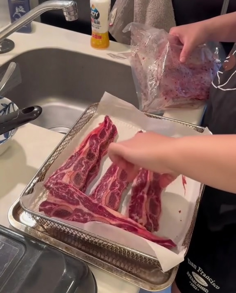 Côtelettes de bœuf crues positionnées dans un panier de friteuse à air, prêtes pour le processus de cuisson.
