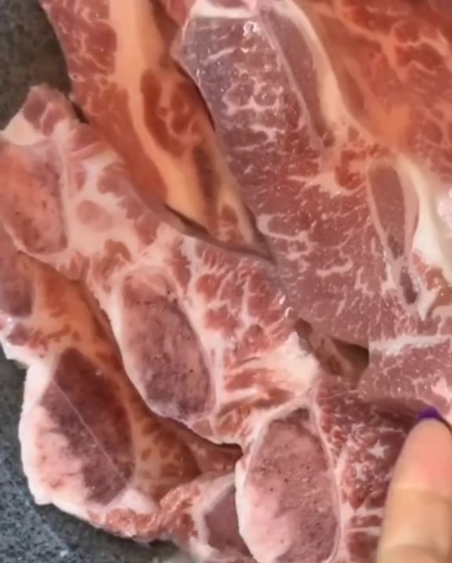 Côtelettes de bœuf crues disposées dans un bol sombre.