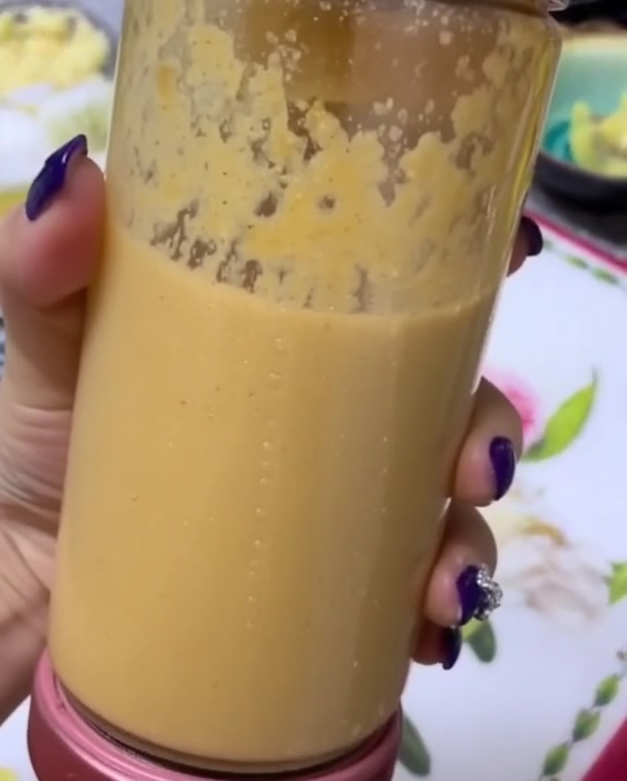 Une main tenant un bol de mixeur transparent rempli dune purée de fruits et légumes lisse et épaisse.